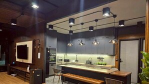 A modern kitchen with a central island, pendant lighting, and a seating area with benches. - Black Sheep House Khao Yai (Pak Chong)