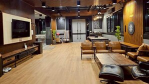 A spacious living area with a large flat-screen TV, leather sofas, a coffee table, and a dartboard. - Black Sheep House Khao Yai (Pak Chong)