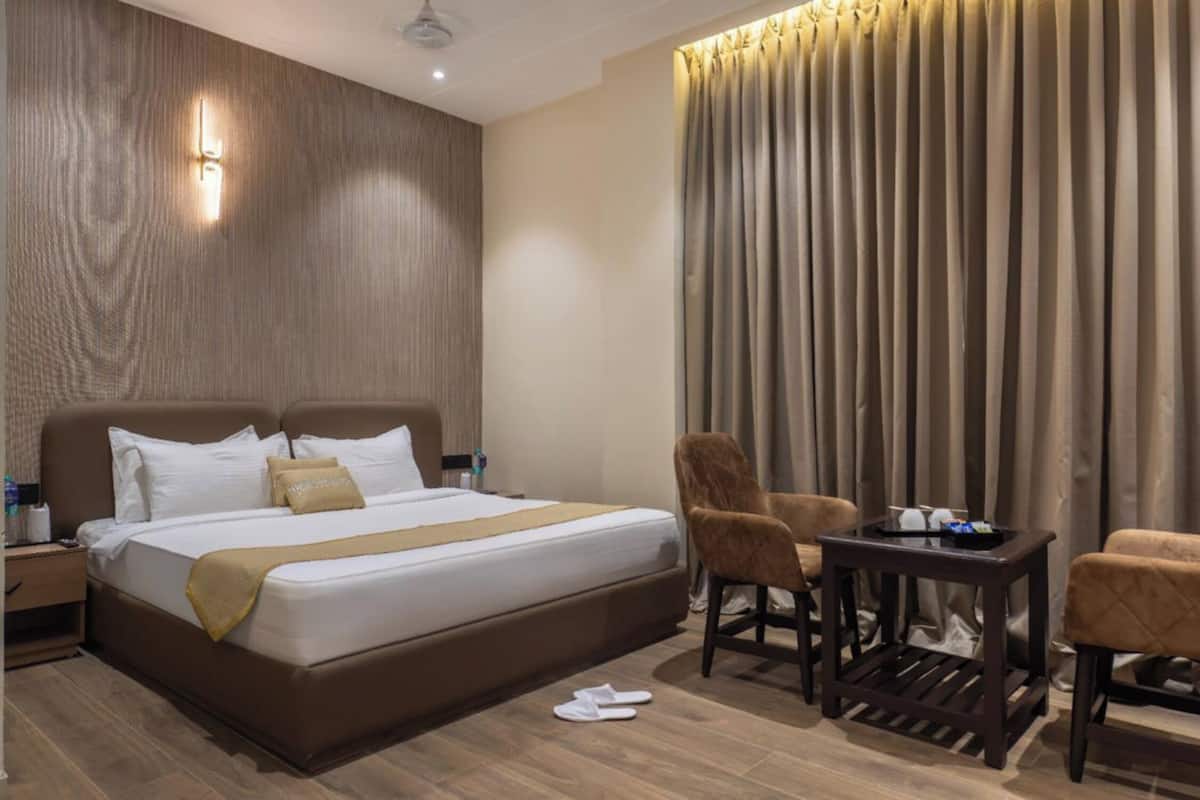 Una habitación de hotel con una cama grande, dos sillas, una mesita pequeña y una mesita de noche.