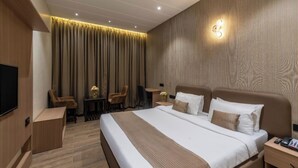 A hotel room with a large bed, a desk, a chair, a TV, and a wall-mounted light fixture. - Hotel Kingsway Continental Raipur (Raipur)