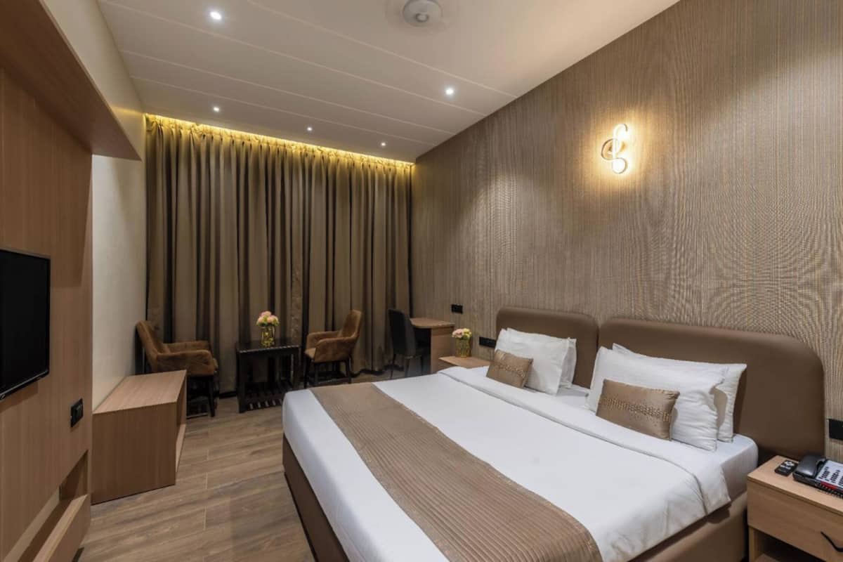 Habitación de hotel con una cama grande, un escritorio, una silla, un televisor y una lámpara fijada a la pared.