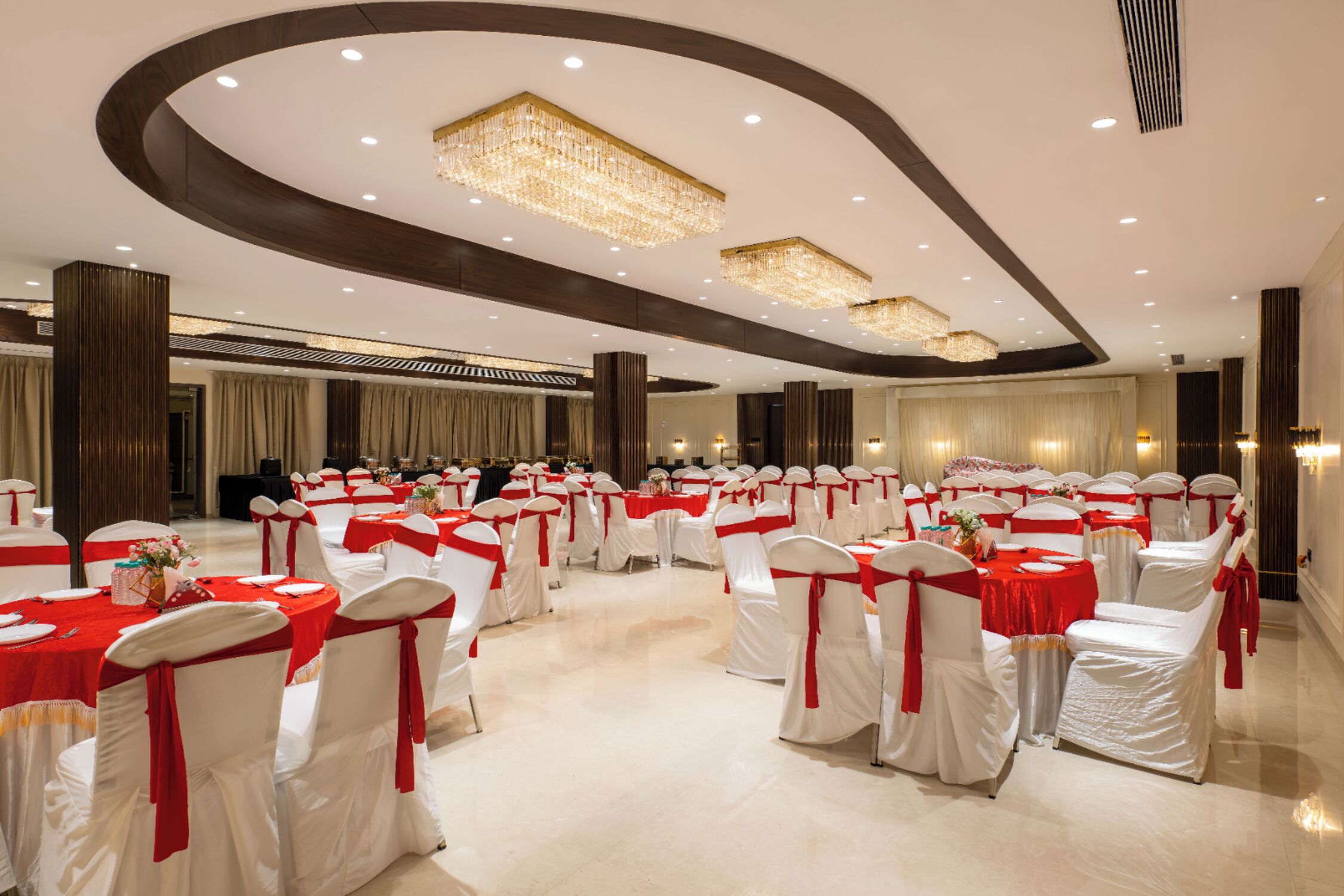 A large banquet hall with round tables and white chairs, each with red sashes.