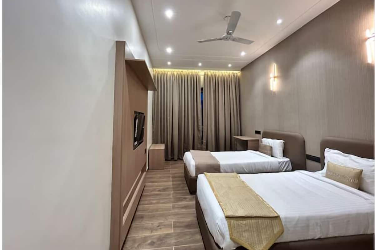 Habitación de hotel con dos camas, ventilador de techo, mesita de noche y un gran ventanal con cortinas.