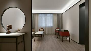 A modern hotel room with a round mirror, a small table, a sofa, and a dining area with chairs.