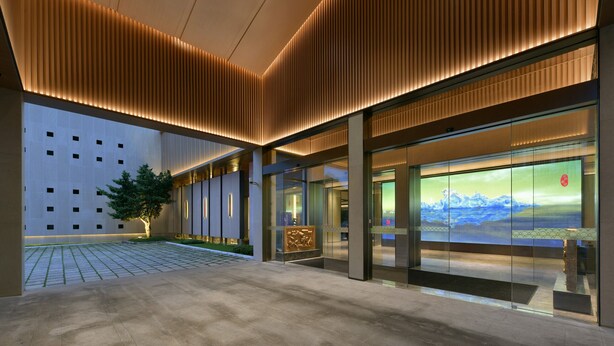 A modern building with a glass facade, a courtyard with a tree, and a large digital display.