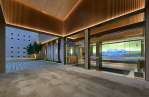 A modern building with a glass facade, a courtyard with a tree, and a large digital display. - JOYA Hotel Shanghai Jiading (Shanghai)