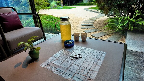A table with a Go board, a water bottle, and a bowl of stones, set against a window overlooking a garden path. - JOYA Hotel Shanghai Jiading (Shanghai)