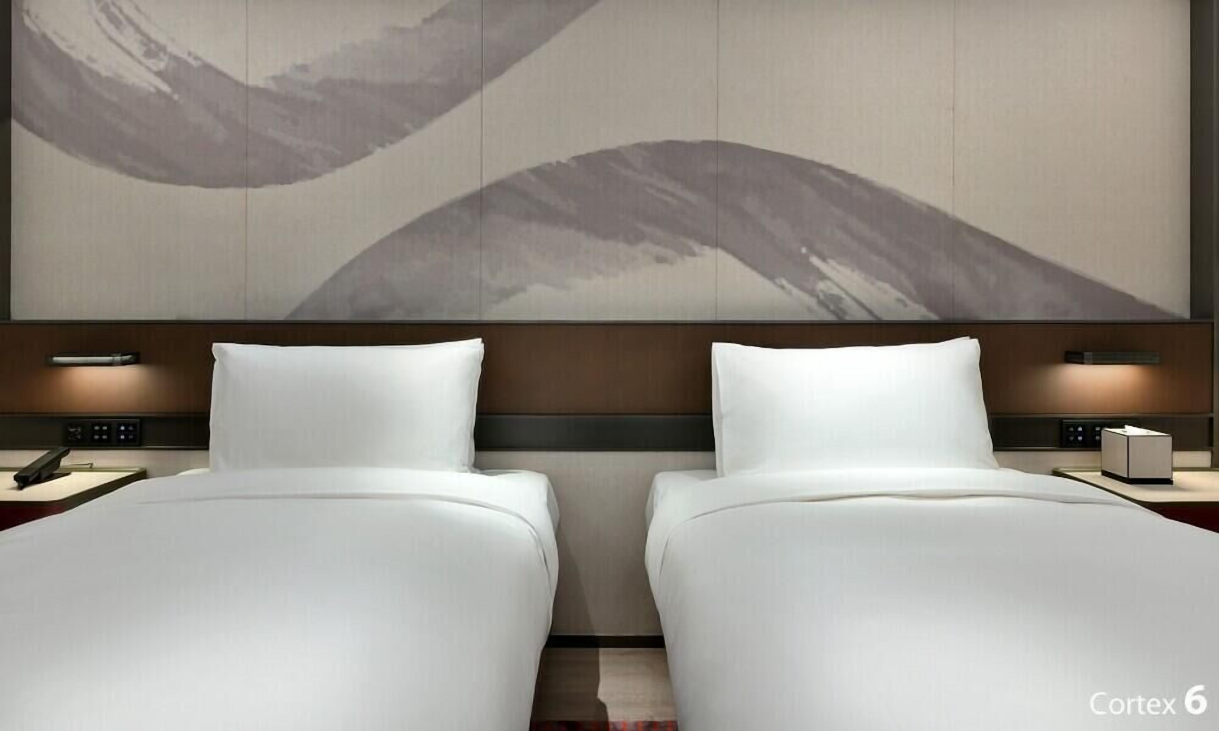 Habitación de hotel con dos camas, una gran obra de arte abstracta en la pared, mesitas de noche con lámparas y un panel de control.