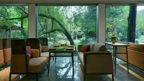 A modern interior with a large window overlooking a lush garden. There is a dining area with a table and chairs, and a seating area with a sofa and armchairs.