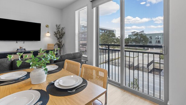 A modern dining area with a large window, a flat-screen TV, and a balcony with a view of the city. - Lux King Suite | Pool | Gym | By Domain Mall | TechRidge (Austin)