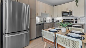 A modern kitchen with stainless steel appliances, light wood cabinets, and a dining area with a wooden table and wicker chairs. - Lux King Suite | Pool | Gym | By Domain Mall | TechRidge (Austin)