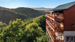 Une cabane en rondins à plusieurs étages, dotée de balcons et entourée d’une forêt dense et de collines.