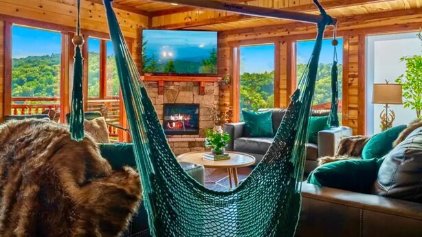 Une pièce chaleureuse avec un hamac, une cheminée et une vue sur la forêt.