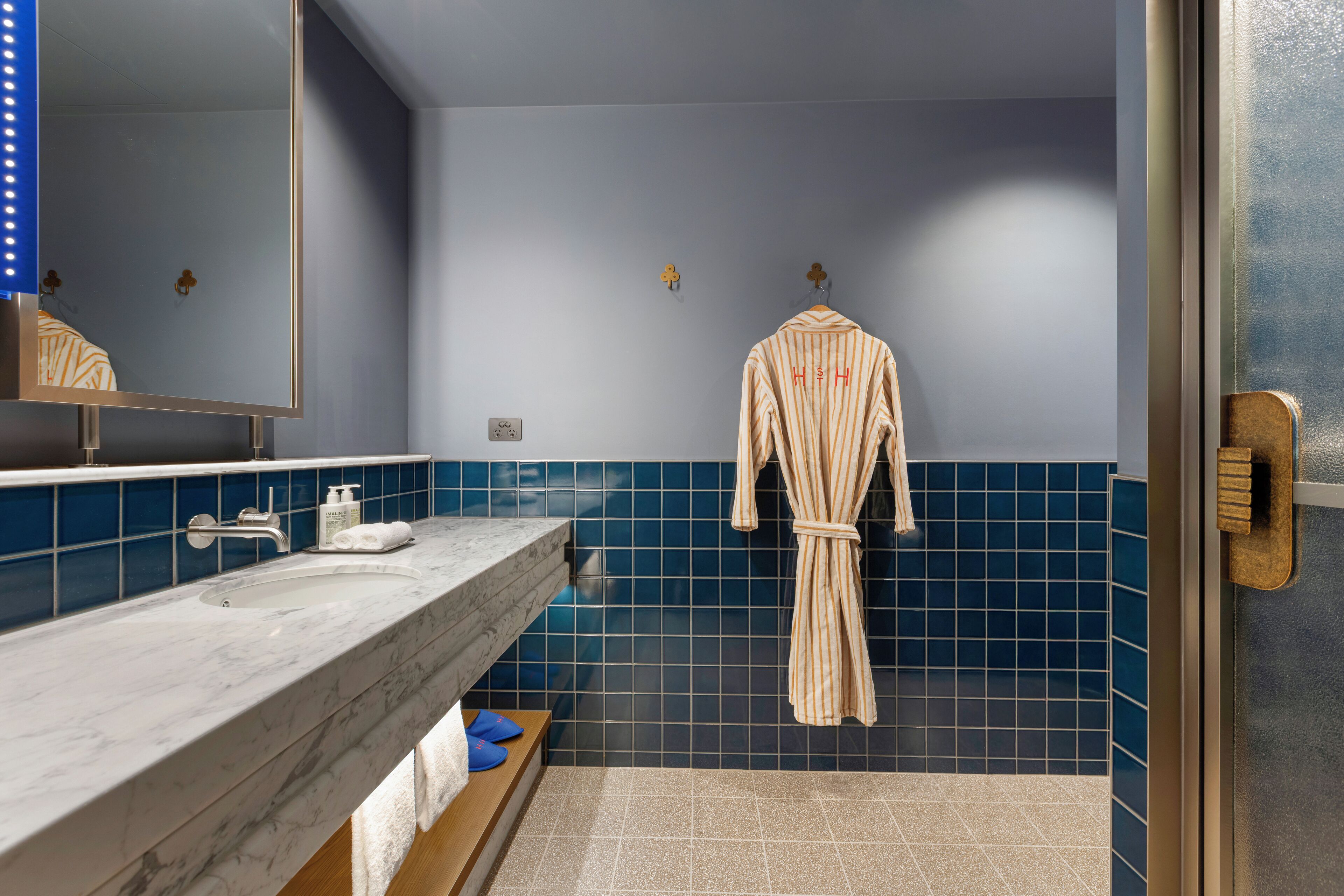 A bathroom with a marble sink, blue tiles, and a robe hanging on the wall.