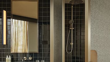 Un baño con un espejo grande, ducha con cabezal de ducha manual, lavamanos con artículos de tocador y un perchero para toallas.