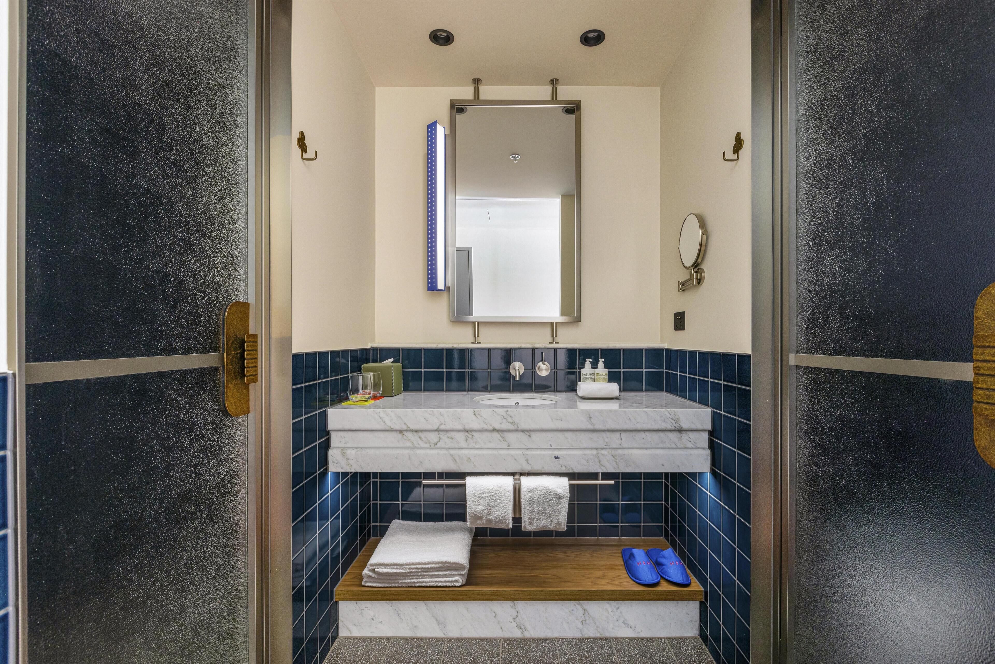 A bathroom with a glass door, a marble sink, a mirror, and a towel rack.
