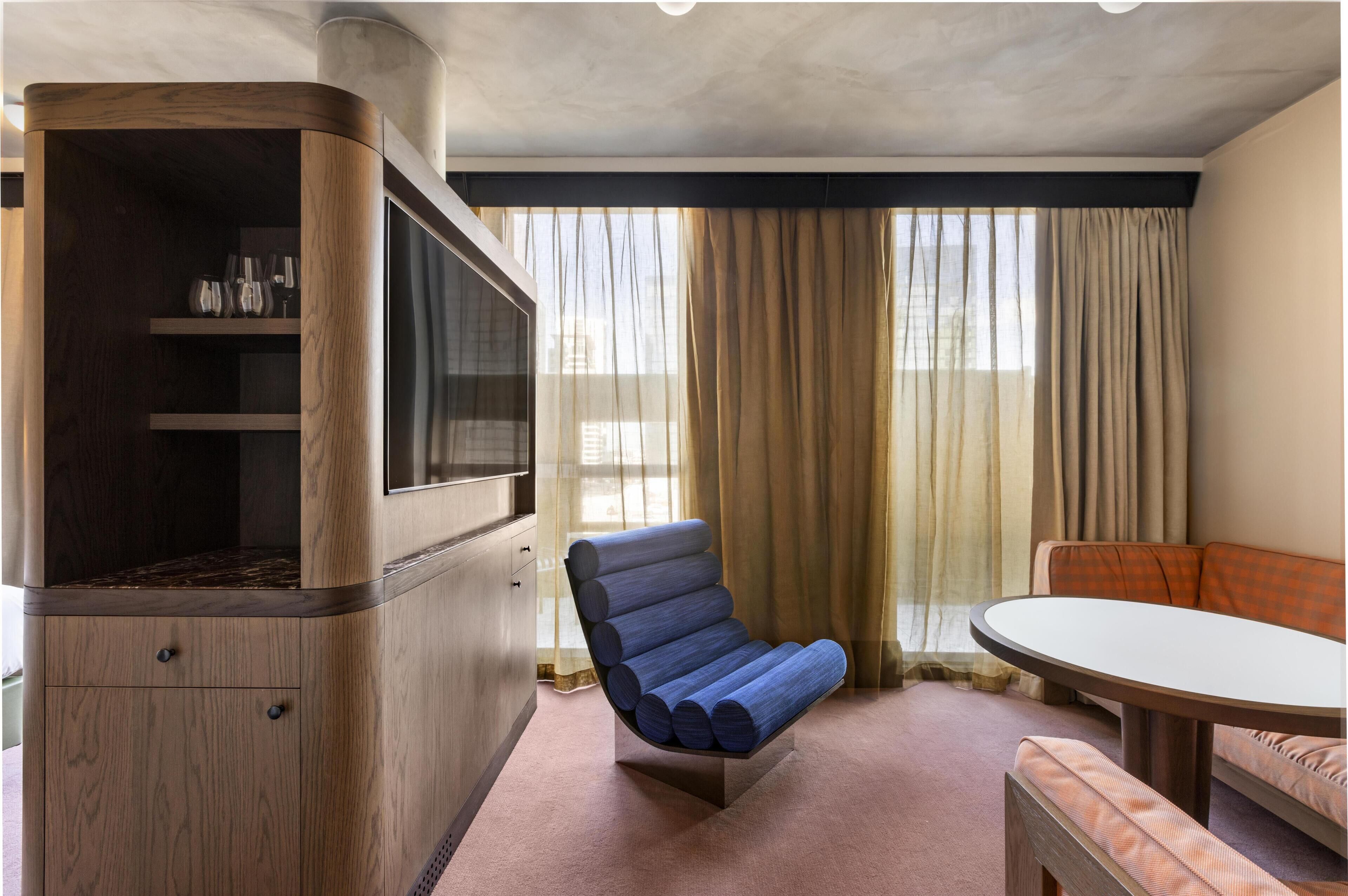 A modern room with a built-in TV, a blue cushioned chair, a round table, and a sofa.