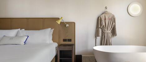 Habitación de hotel con cama, lámpara de noche, bata y bañera independiente.
