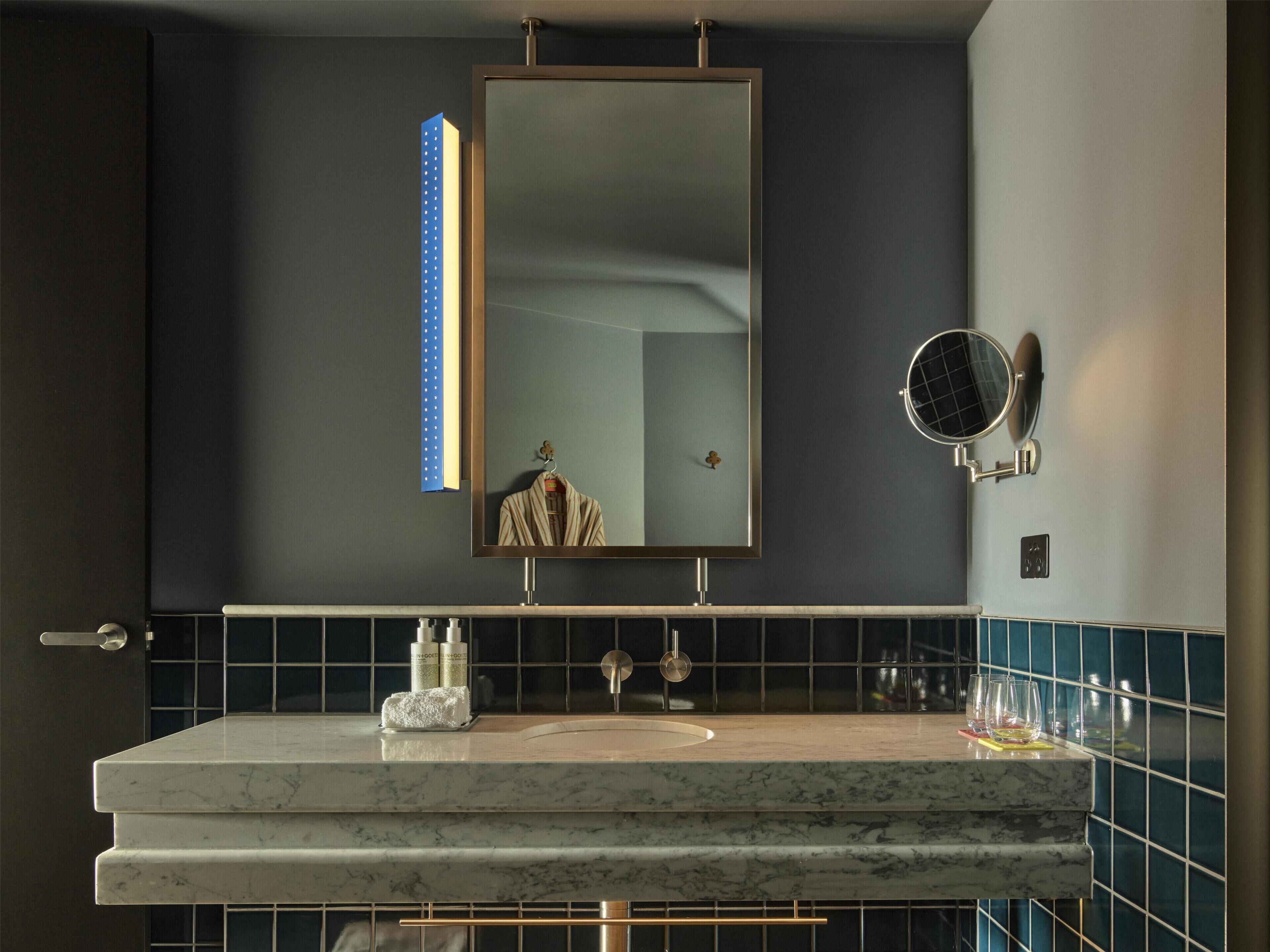 A bathroom with a large mirror, a round mirror, a marble sink, and a towel rack.