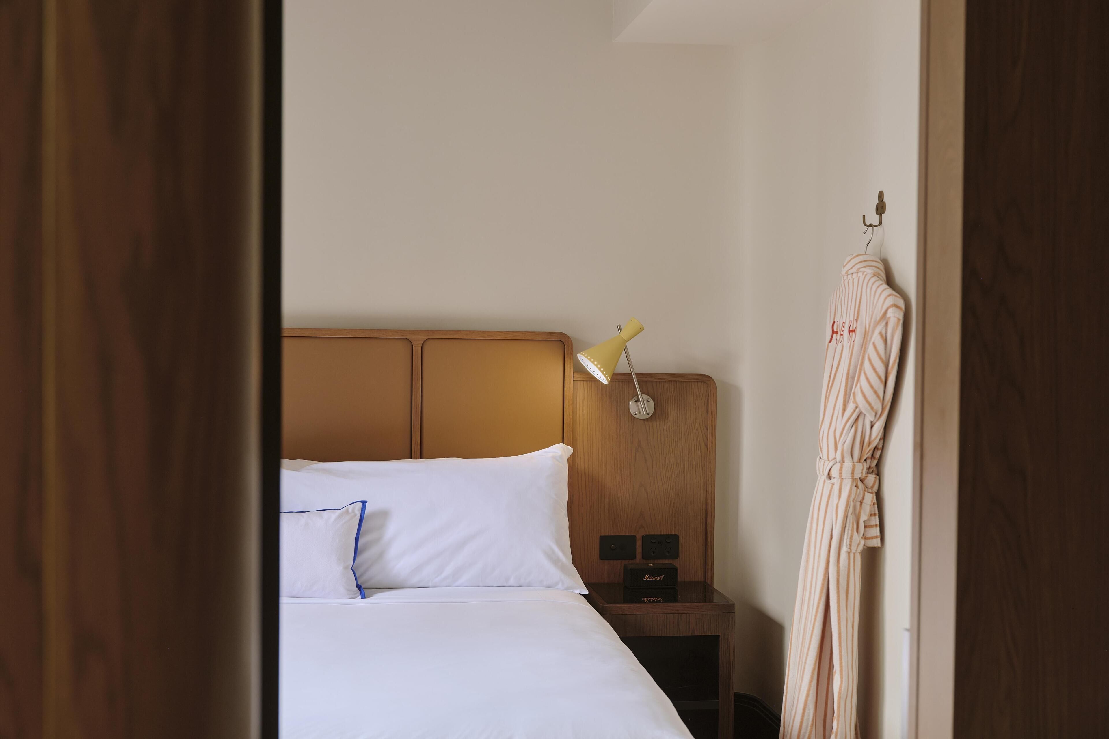 A hotel room with a bed, a bedside lamp, a nightstand, and a robe hanging on a hook.