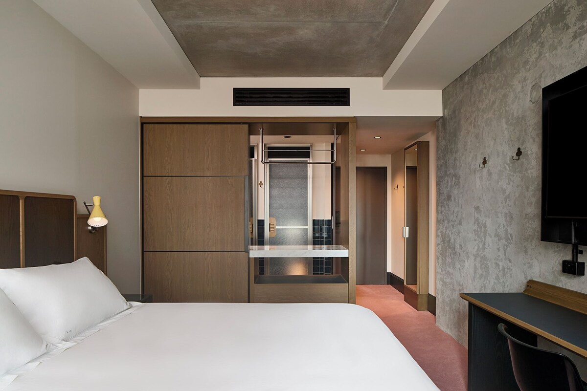 Quarto de hotel moderno com uma cama grande, uma mesa e um guarda-roupa.