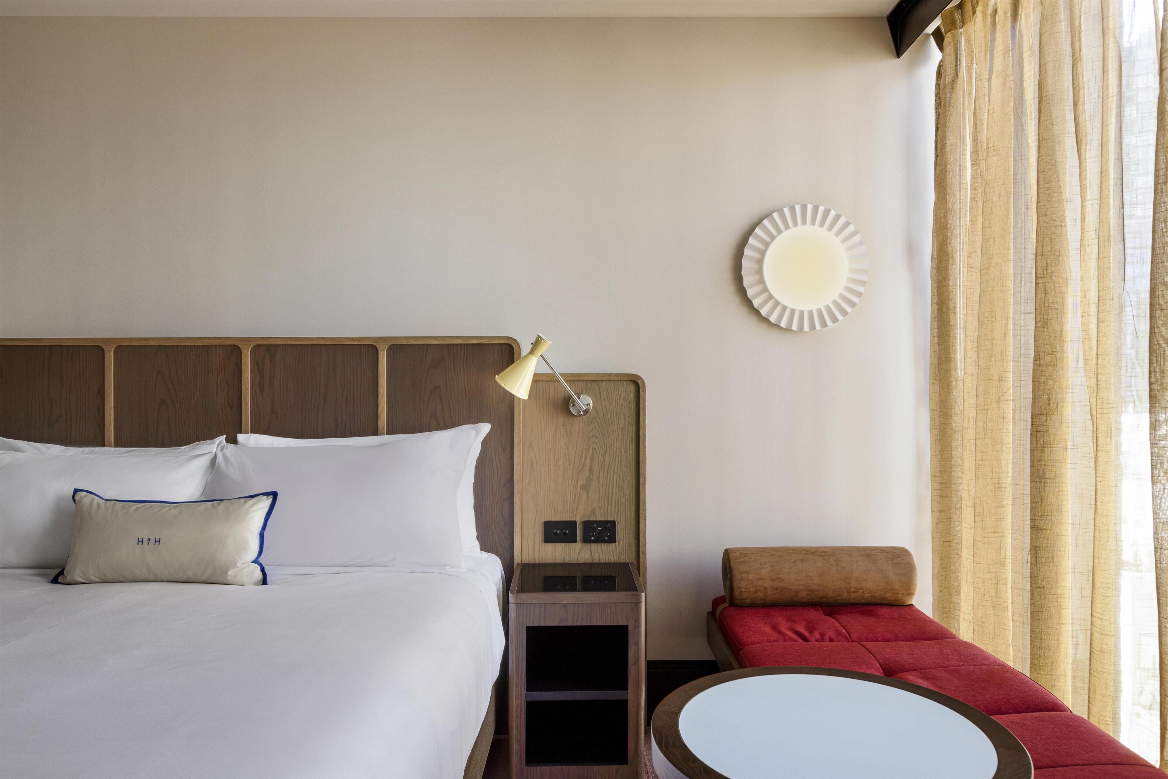 A hotel room with a bed, bedside table, lamp, wall clock, and a red sofa.