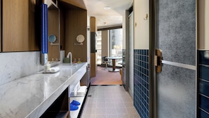 A modern bathroom with a marble countertop, a sink, a mirror, and a shower area. - Hannah St Hotel Melbourne (Southbank)