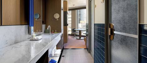 A modern bathroom with a marble countertop, a sink, a mirror, and a shower area.