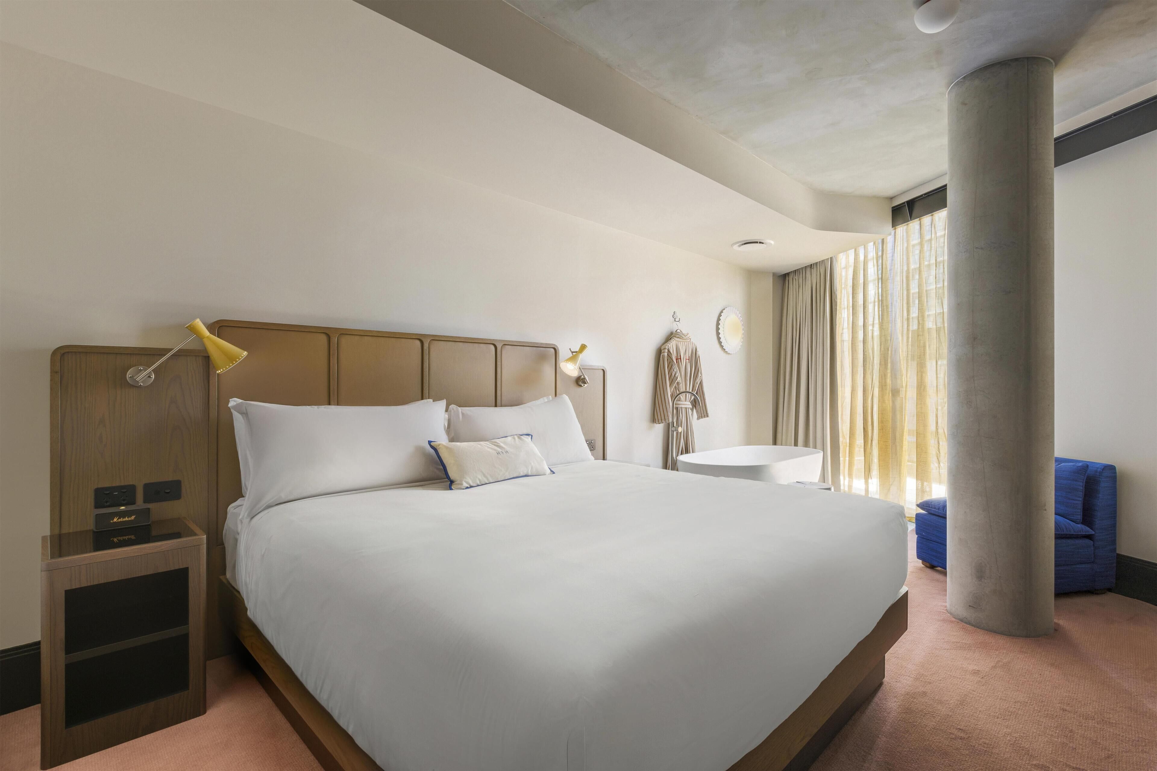 A hotel room with a large bed, bedside lamps, a round table, and a blue chair.