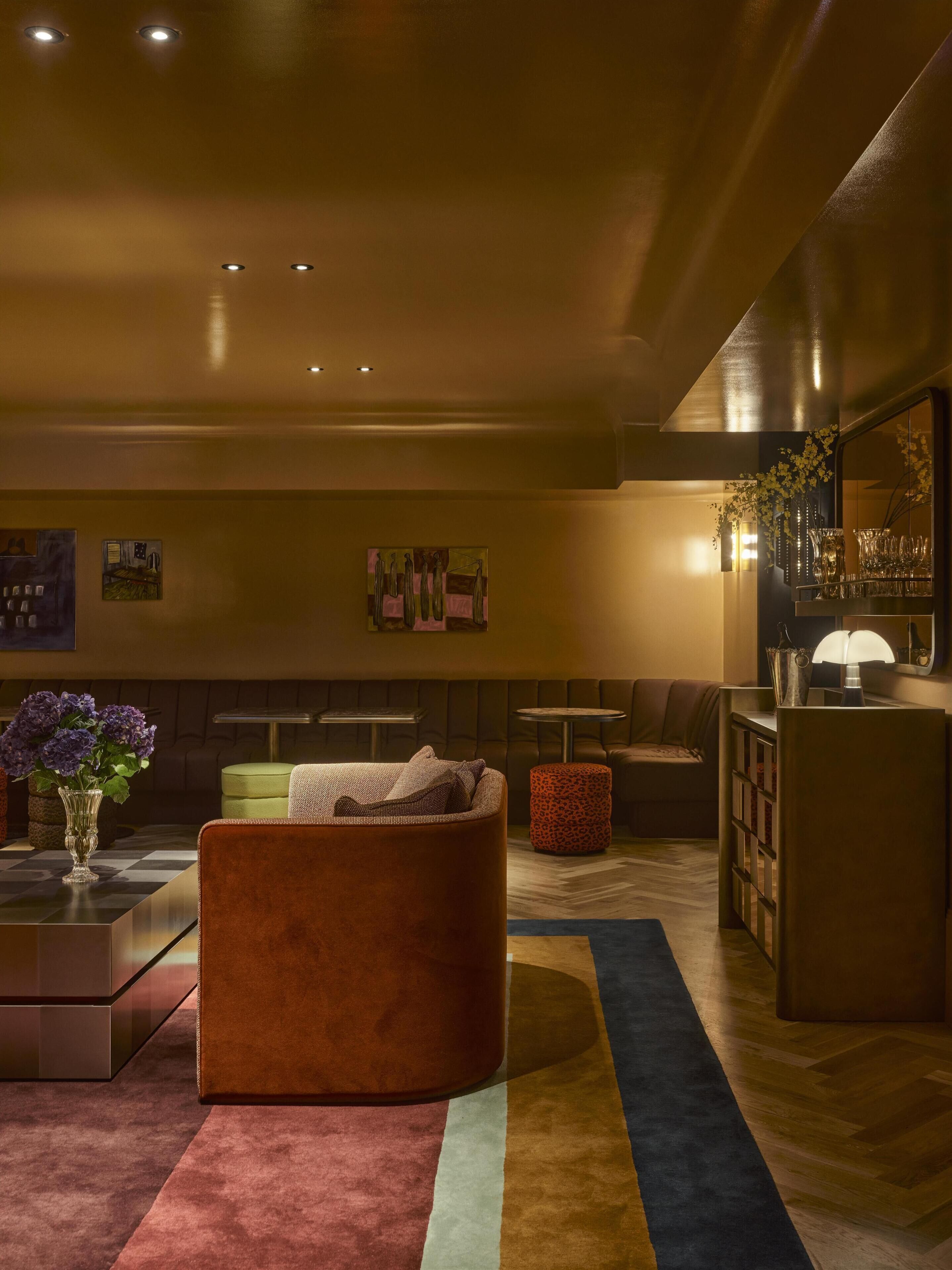 A modern living room with a sofa, a coffee table, a patterned rug, and a bar area with glasses and a vase.