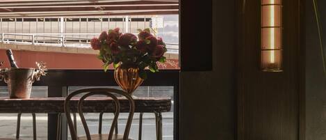 A restaurant interior with a view of a parking garage, a table with chairs, a vase with flowers, and a wall-mounted lamp.