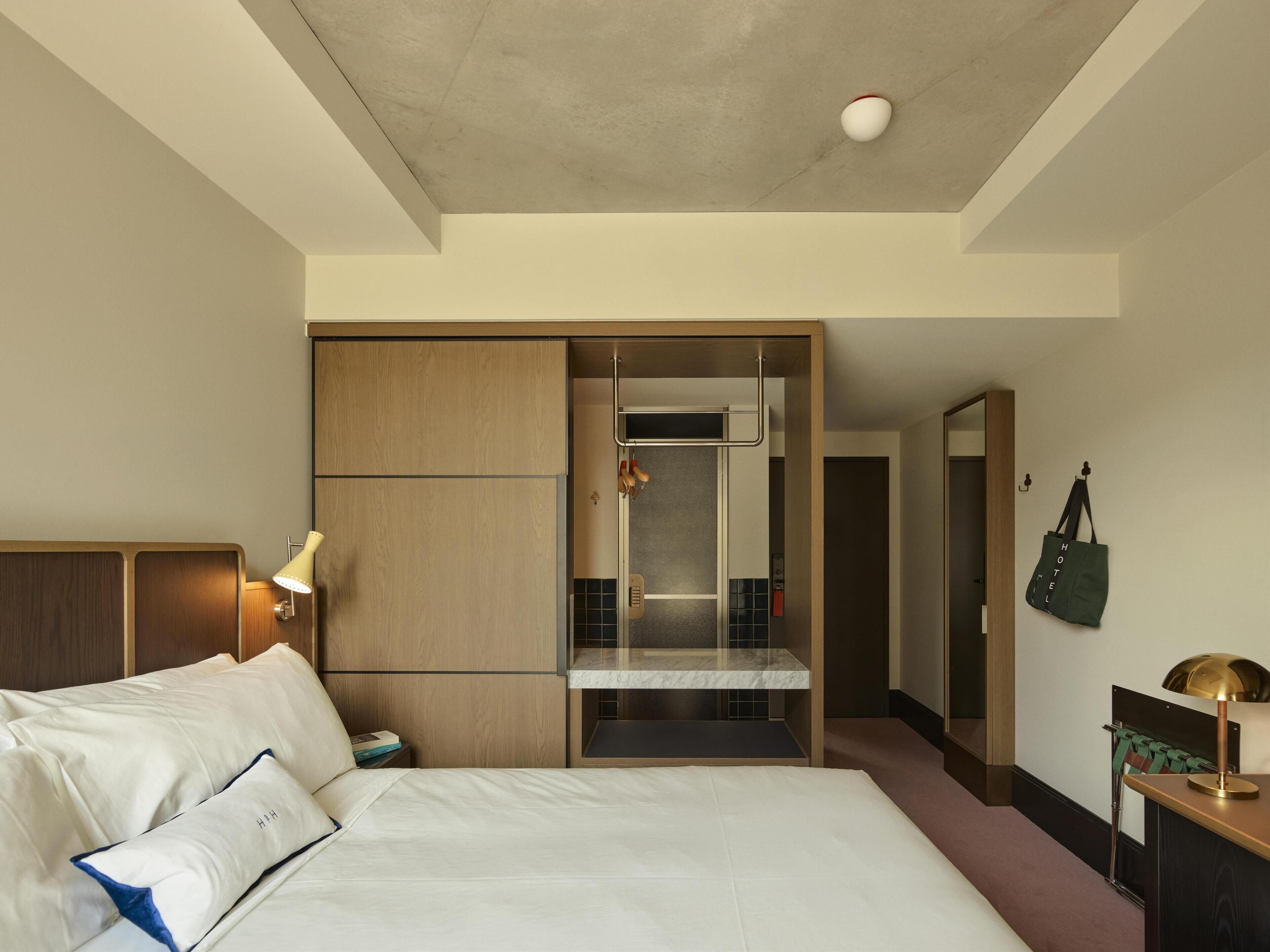 A hotel room with a bed, a desk, a mirror, a wardrobe, and a bathroom visible through a sliding door.