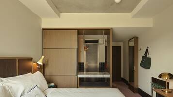 A hotel room with a bed, a desk, a mirror, a wardrobe, and a bathroom visible through a sliding door.