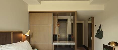 A hotel room with a bed, a desk, a mirror, a wardrobe, and a bathroom visible through a sliding door.