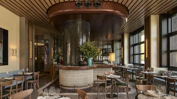 Een restaurantinterieur met een centrale bar, zithoekjes en een decoratief plafond.