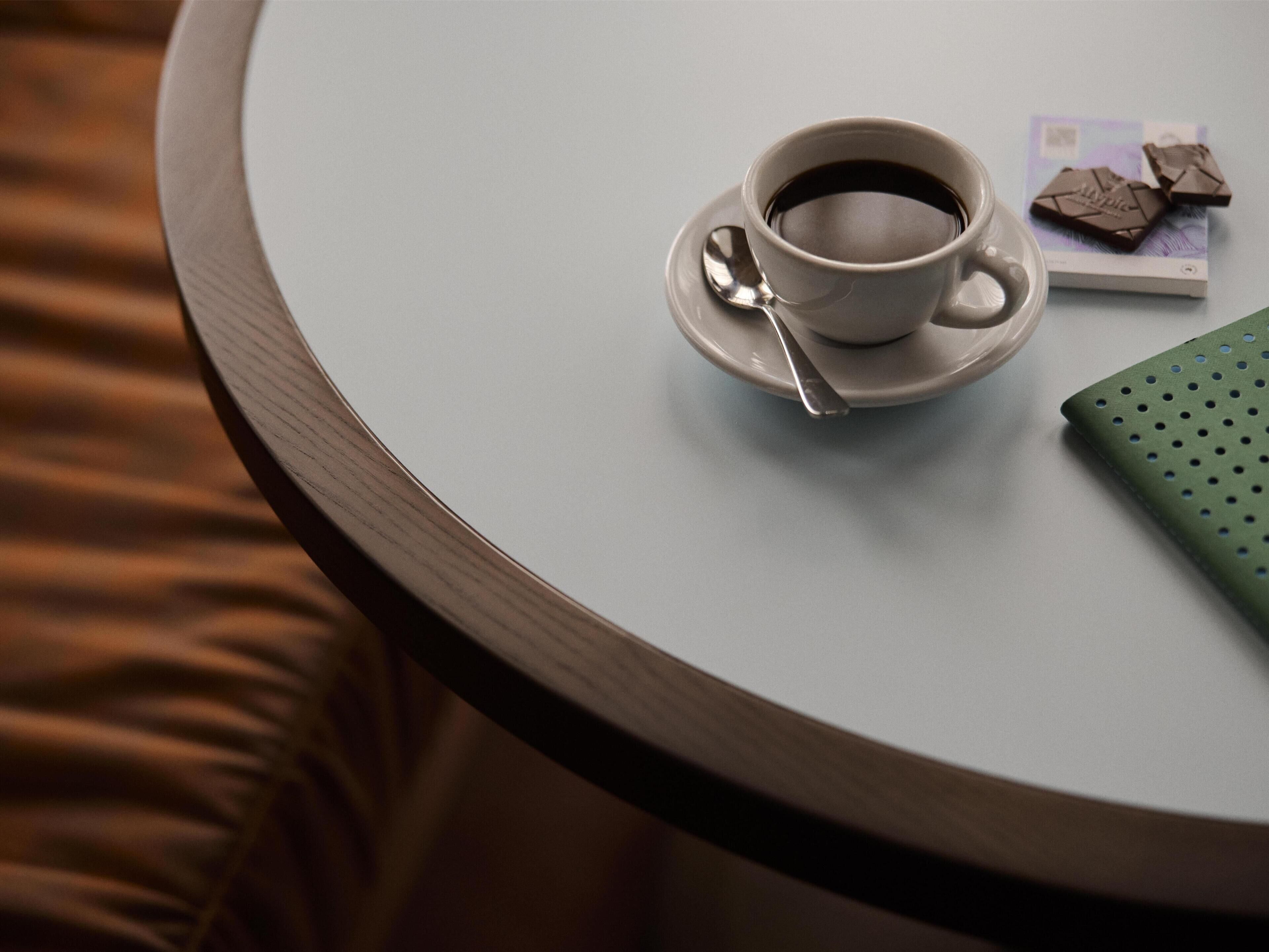 A round table with a cup of coffee, a spoon, and a chocolate bar.