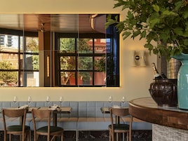 A restaurant with a view of a building through a window, a bench seating area, and a vase with a bottle on a counter.