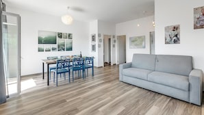 A modern living room with a grey sofa, a dining area with blue chairs, and a wooden floor. - Casa Tramonti: Mountain-View with Terrace Dining, Gemonio, Italy (Gemonio)