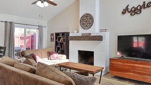 Una sala de estar con sofá, mesa de centro, chimenea, televisor y ventilador de techo.