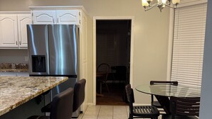 A modern kitchen with a stainless steel refrigerator, a marble countertop, and a dining area with a glass table and black chairs.