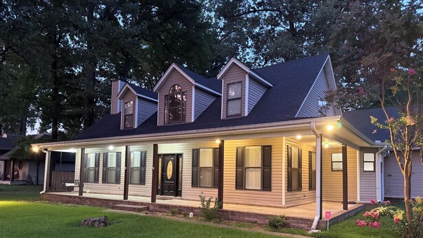 A two-story house with a covered porch, a front door, and a small front yard with grass and a tree.