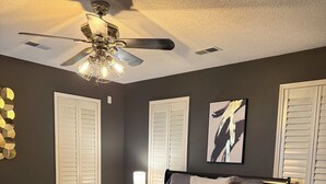 A bedroom with a bed, a ceiling fan, and a nightstand.
