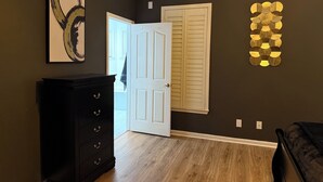 A room with a dark wall, a wooden floor, a black dresser, a white door, and a wall art piece.