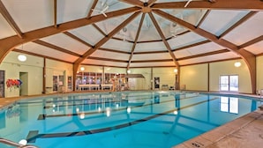 An indoor swimming pool with a high ceiling and wooden beams, clear pool lanes, and a visible entrance.