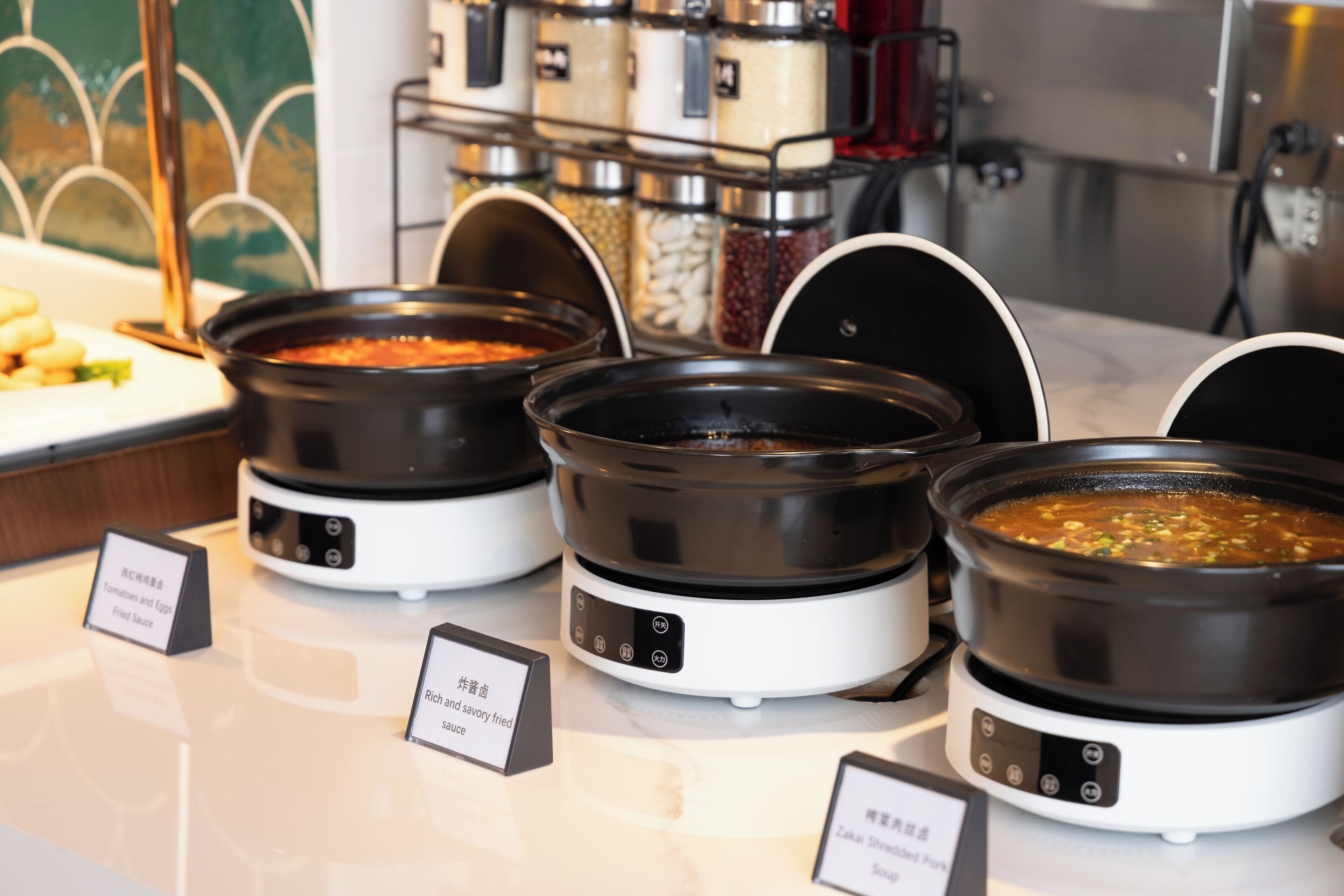 Three electric pressure cookers on a countertop with labels indicating different sauces.