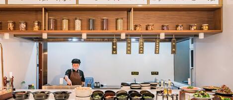 Un restaurant où un chef prépare les plats, où différentes spécialités sont présentées et où des œuvres d’art traditionnelles ornent les murs.