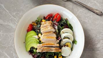 A white plate with a salad, including avocado, tomatoes, and boiled eggs, on a marble surface.