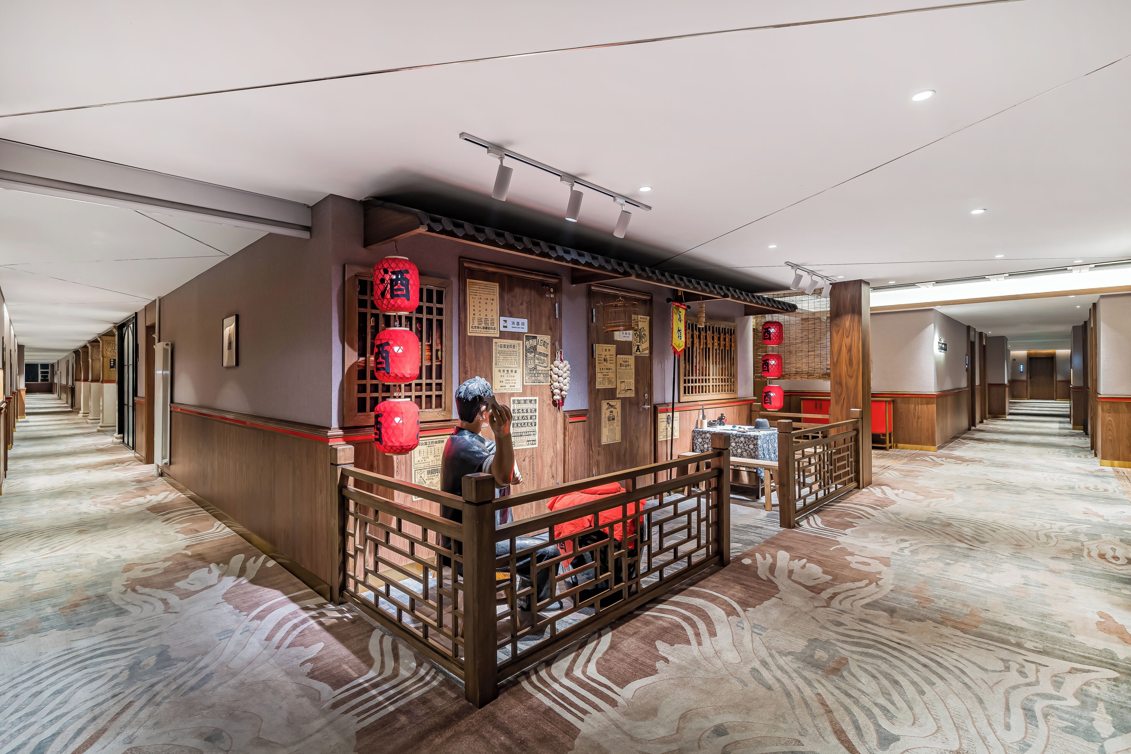 A hotel lobby with a traditional design, featuring a wooden reception desk, red lanterns, and a patterned carpet.