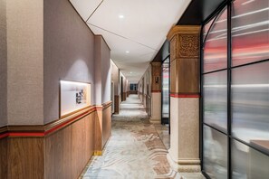 A corridor with wooden paneling, a patterned carpet, and a glass partition on one side.