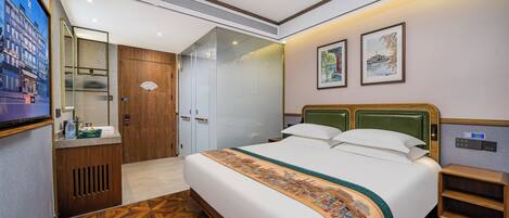 Habitación de hotel con cama, tocador, espejo, puerta y televisor montado en la pared.